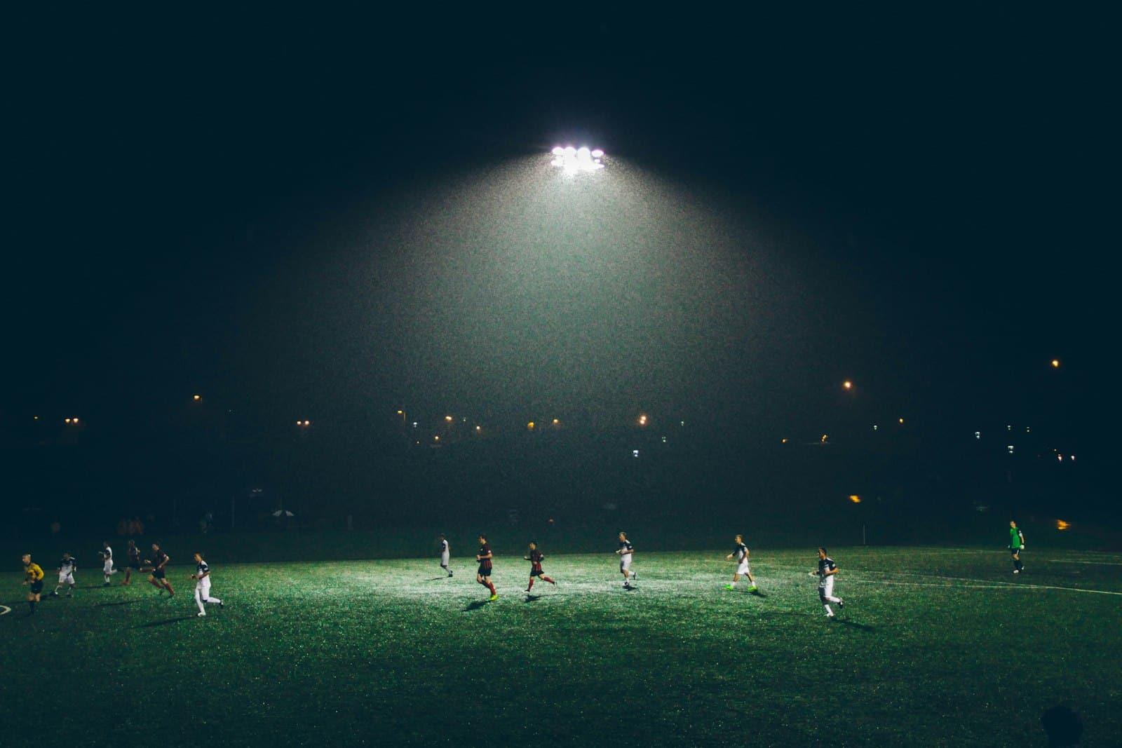 Partido de fútbol nocturno bajo un reflector, con jugadores en la cancha