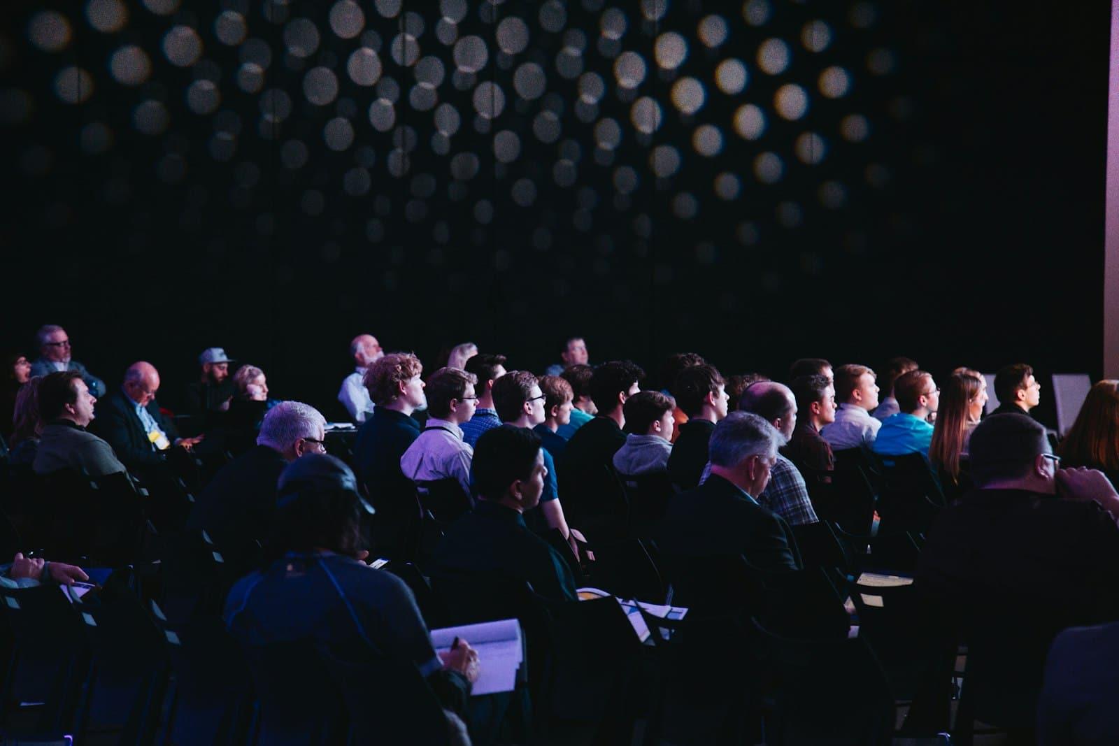 Público sentado atento a una conferencia en un auditorio oscuro