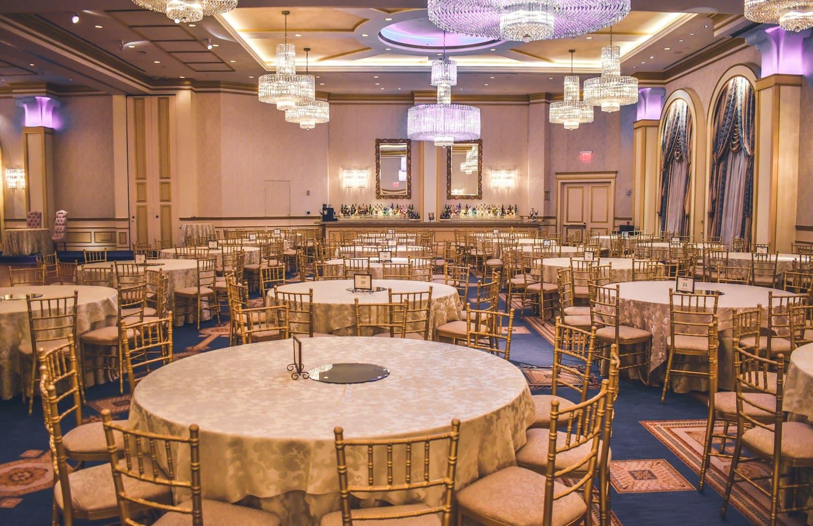 Salón de eventos con mesas redondas armadas y arañas de cristal